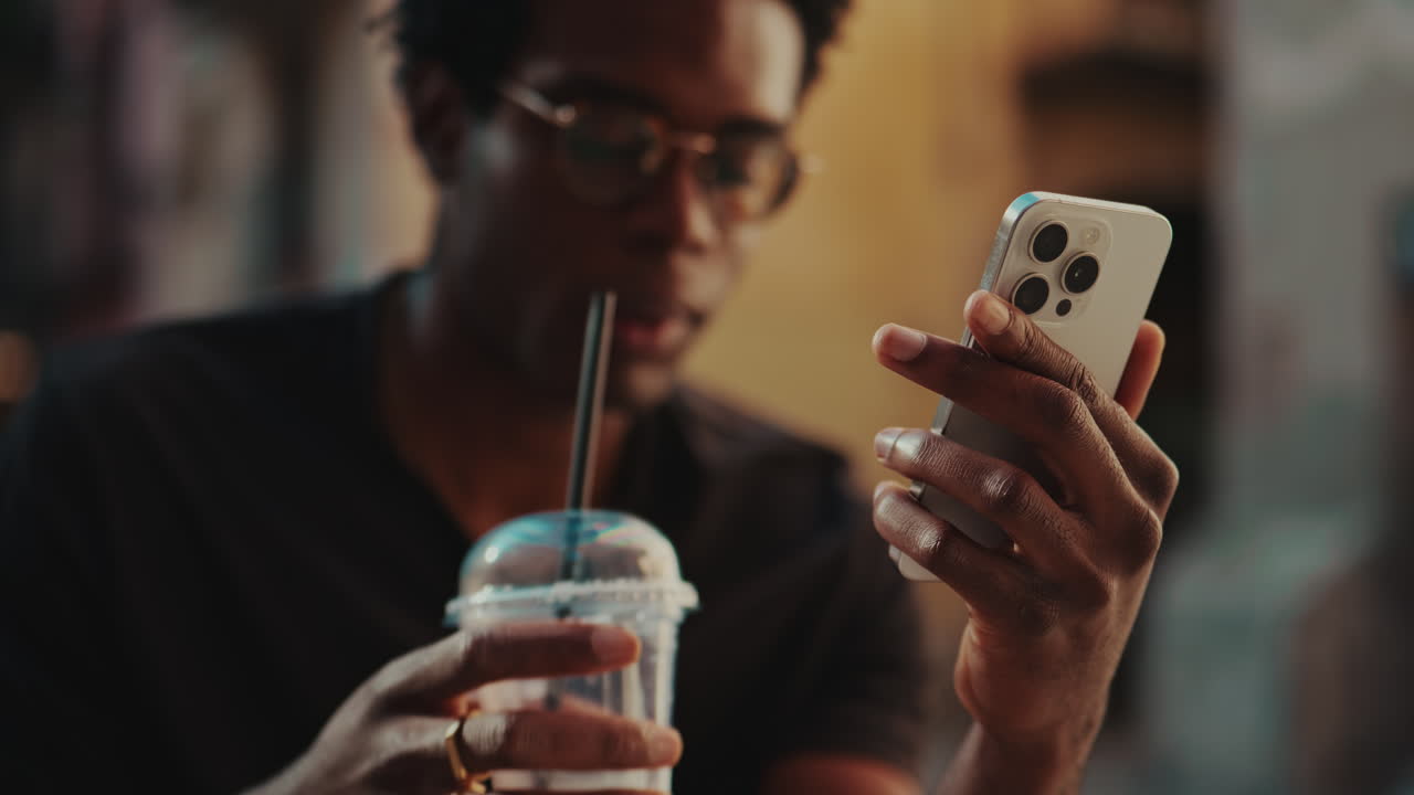 Giovane uomo afroamericano che naviga sullo smartphone e beve