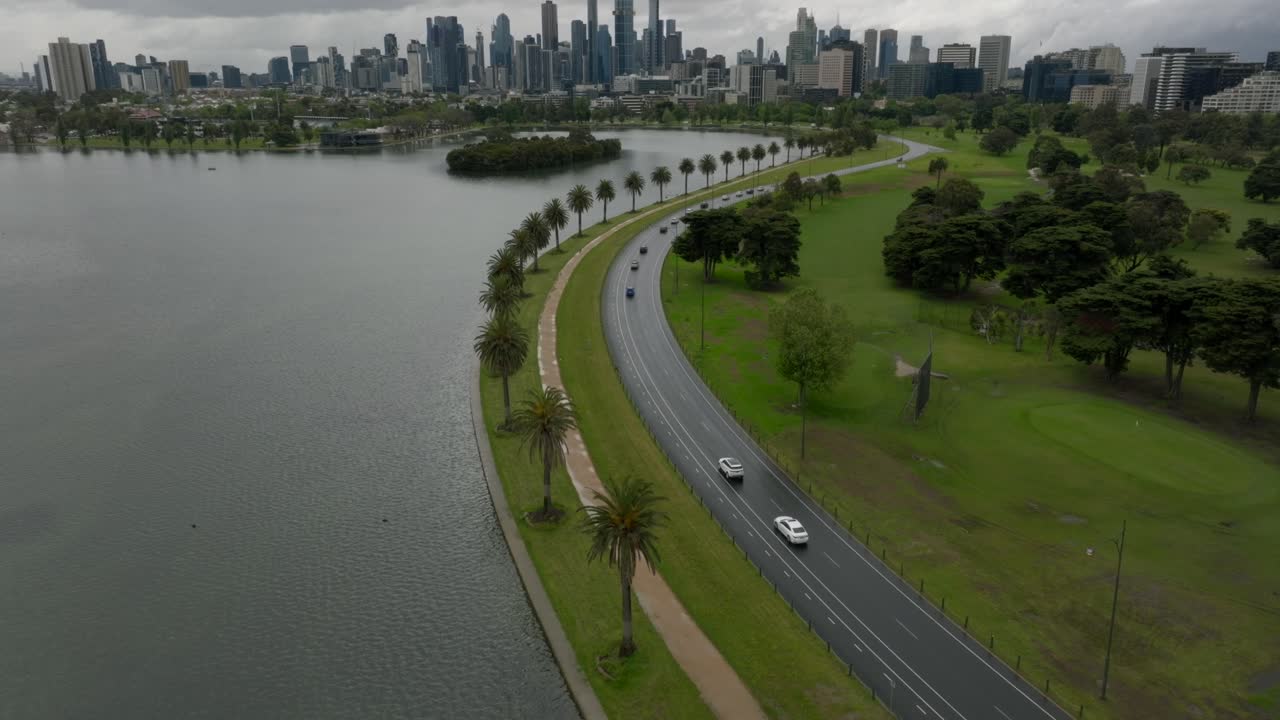 Slow pan up to show Melbourne's business district from Albert Park, while cars are passing by on the park's road