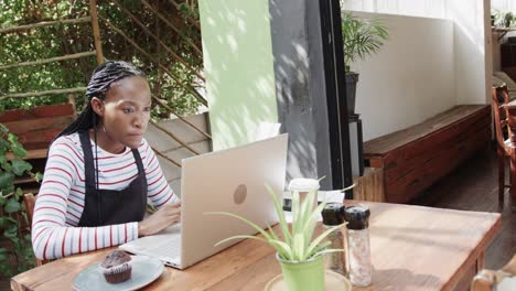 propietaria de una cafetería afroamericana usando una computadora portátil y haciendo papeleo afuera, en cámara lenta