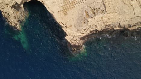 aerial overhead reveal shot of the limestone cliffs with salt pans near canyon wied il-għasri with a beautiful clear turquoise water