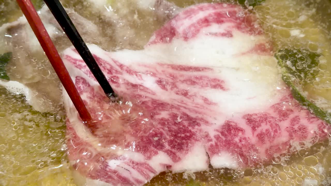 Marbled wagyu beef slices simmer in bubbling broth, close-up view, bright lighting, minimal camera movement