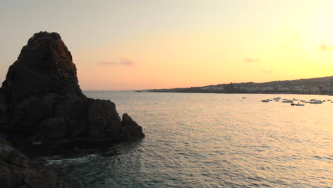 aerial circle around small rock island revealing beautiful coastal town and sunset