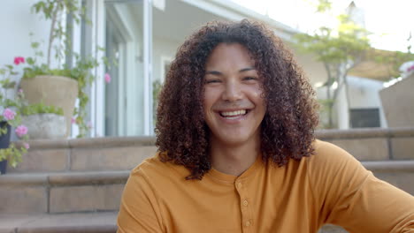 portrait of happy biracial man with long curly hair smiling in sunny garden, slow motion