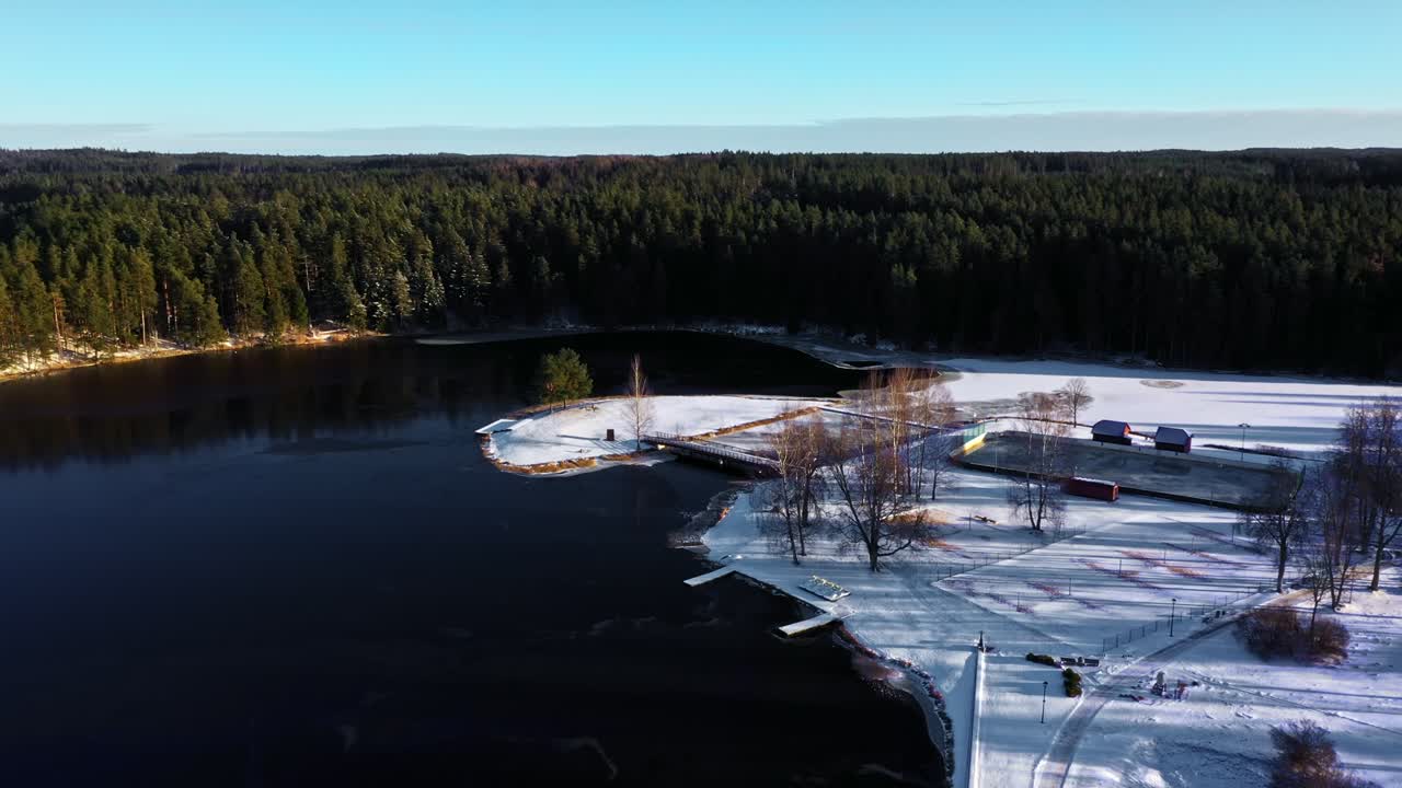 Talvinen rantamaisema jäätyneellä järvellä, lumipeitteisellä saarella ja metsäisellä rannalla kylmänä vuodenaikana.