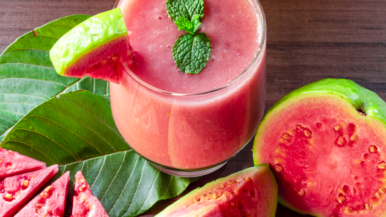 Bicchiere di succo di guava rosso e fette di guava su sfondo di legno