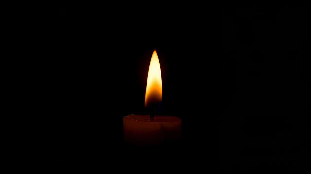 Ripresa di una singola candela di cera con stoppino che mostra lo sfarfallio naturale mentre la fiamma si allunga in uno studio buio