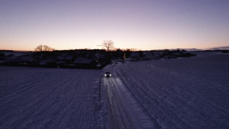 drone view of car driving on snowy road in scandinavian winter landscape - dolly shot