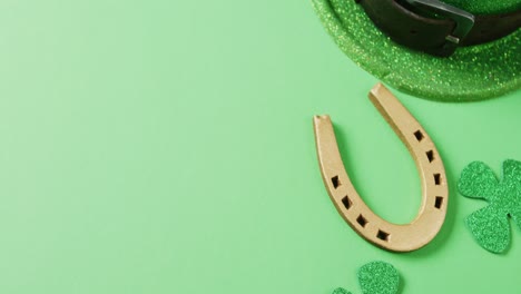 Video-of-st-patrick's-green-shamrock-leaf,-horse-shoe,-hat-with-copy-space-on-green-background