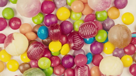 colorful dragee candies, lollipops, bonbons on white background, move in circle, top view close-up. summer bright texture studio shot for store, supermarket. mix of children's sweets made of sugar.