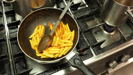 Top-View-Of-Cooked-Penne-Pasta-In-A-Skillet-On-The-Kitchen-Stove-With-Soup-Boiling-In-A-Stainless-Pot---high-angle-orbiting-shot