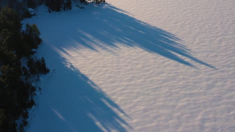 Aerial-tilt-up-from-the-snowy-surface-of-a-lake-to-reveal-camps-and-a-mountain-with-a-lens-flare