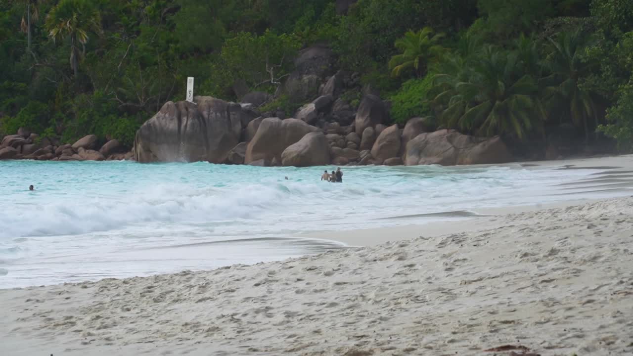 Spiaggia di Anse Lazio sull'isola delle Seychelles con onde e persone che camminano nell'acqua.