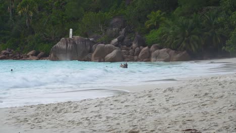 Ans-Lazio-Strand-Auf-Der-Insel-Der-Seychellen-Mit-Wellen-Und-Menschen,-Die-Im-Wasser-Waten