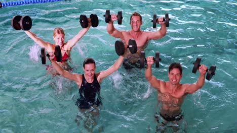 fit people doing an aqua aerobics class in swimming pool with foam dumbbells