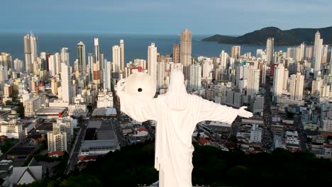 Panel-De-Vista-Aérea-A-La-Derecha-De-Christ-The-Remeeder-En-Balneario-Camboriu,-Brasil-Con-La-Ciudad-Y-El-Océano-Al-Fondo