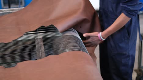 leather being processed by a roller system of machinery in the tannery. - closeup shot