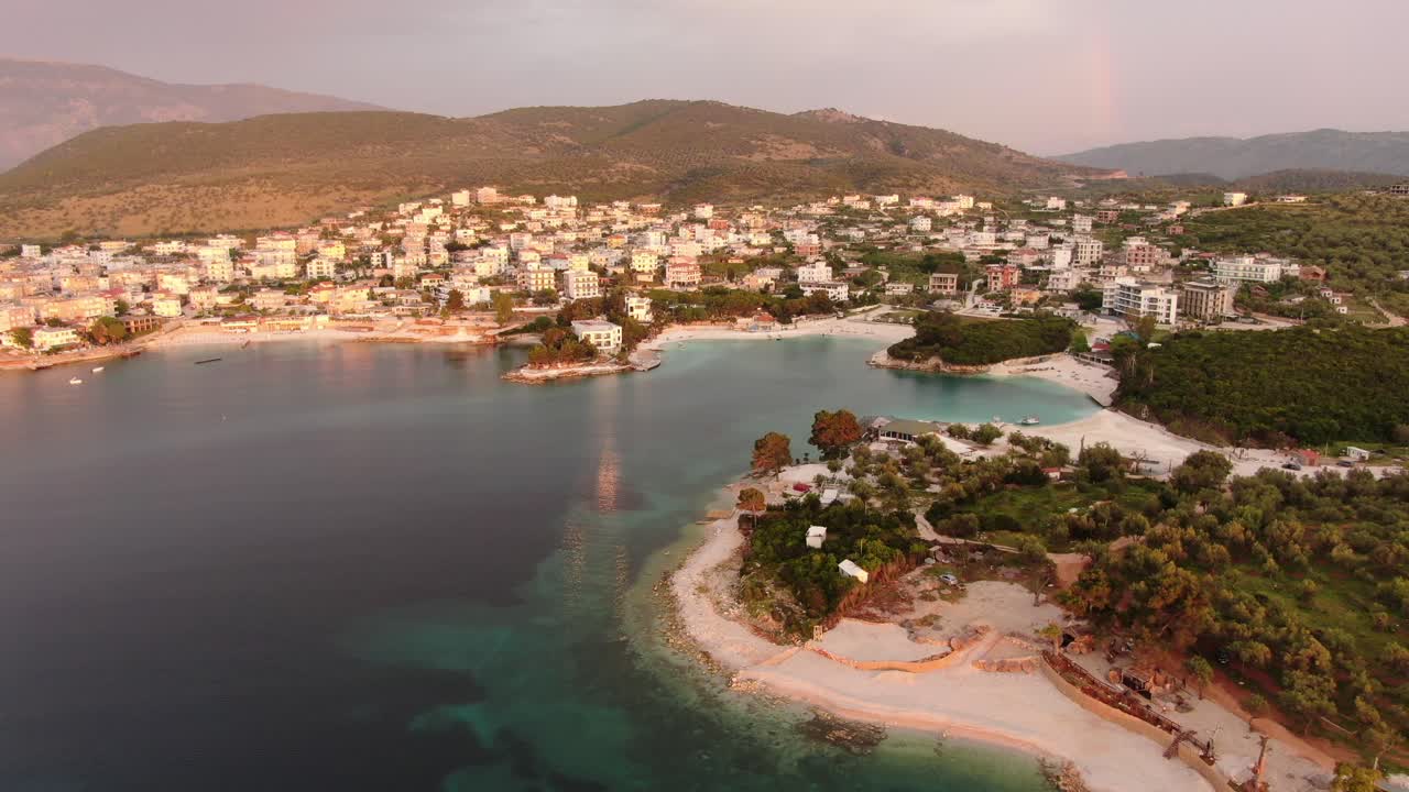 vista de avión no tripulado en albania volando sobre aguas cristalinas azules al atardecer y hoteles con luz roja en ksamil
