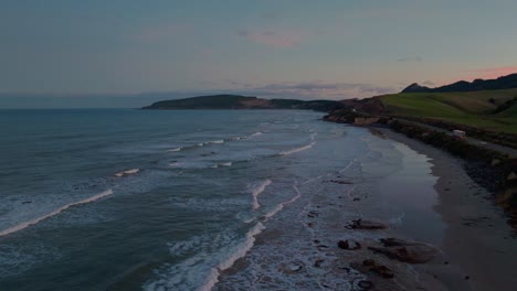 Vista-Panorámica-Inversa-Del-Océano-Con-Suaves-Olas-En-Una-Playa-Escarpada-Durante-La-Puesta-De-Sol-En-El-Destino-De-Katiki,-North-Otago,-Nueva-Zelanda-Aotearoa