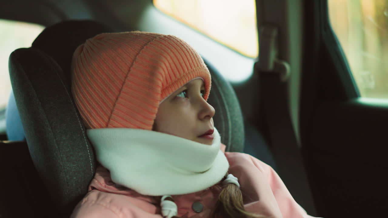 A serene moment of a little girl in a pink cap, jacket, and white winter scarf sitting in a car