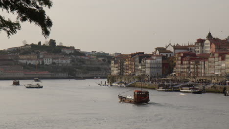 river cruises in douro river with riverside buildings and seagulls in porto, portugal, wide shot
