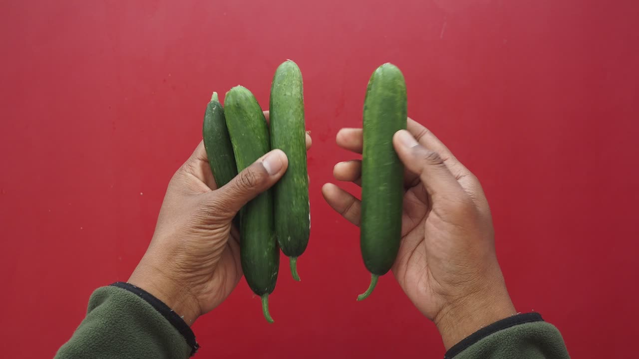 Hands Holding Cucumbers Against a Red Background