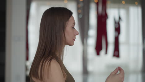 side view of mindful woman closing eyes in yoga studio hands resting on chest and stomach red aerial silks backdrop serene meditation atmosphere with soft natural light mirror reflection
