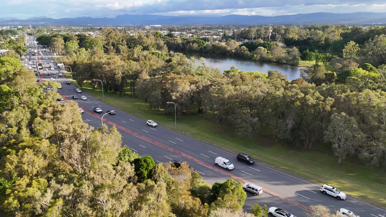 Aerial footage captures vehicles moving along a tree-lined highway in Gold Coast, Australia, under clear skies and natural lighting