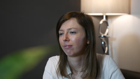 a young woman with a neutral expression listening at home