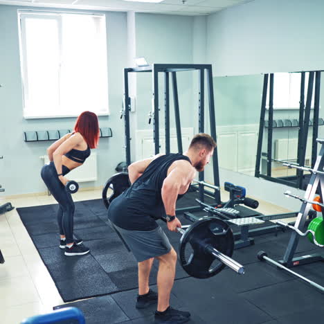 back view of athletic man and woman lifting barbells in the modern gym. strong couple is doing physical exercises with heavy equipment standing in front of a big mirror in fitness club.