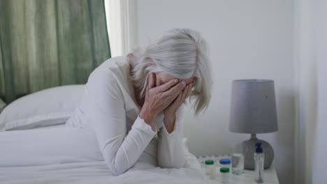 Sick-or-depressed-senior-caucasian-woman-sitting-up-in-bed-at-home-and-holding-her-head