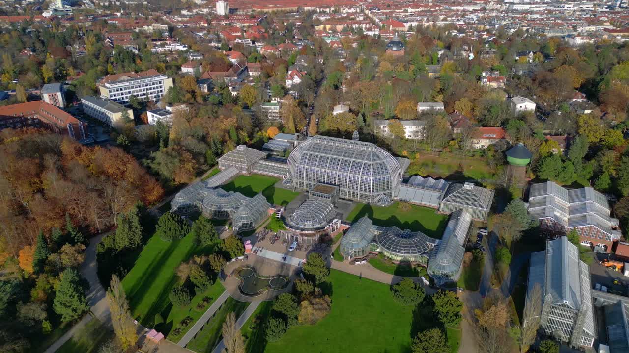 Berlin botanical garden tropical greenhouse glasshouses surrounded by autumn trees and city landscape. speed ramp hyper motion time lapse Dramatic aerial view flight panorama orbit drone