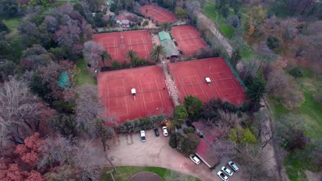 aerial orbit of people playing in red clay tennis courts surrounded by trees and vegetation in o'higgins park, santiago, chile