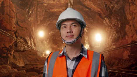 close up of asian male engineer with safety helmet looking around while standing in underground mine tunnel