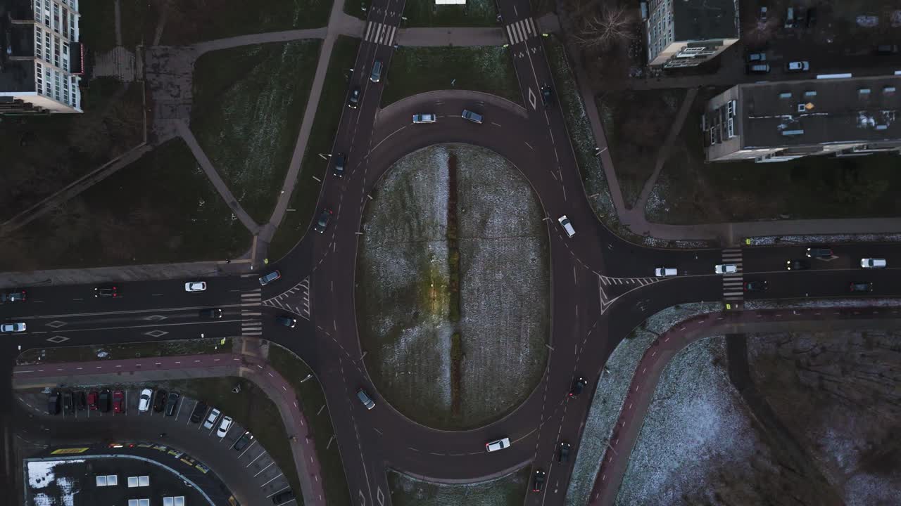 Cars driving on roundabout at evening time, aerial top down view