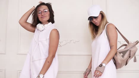 Two-female-hipsters-in-white-dresses-dancing-on-the-background-of-white-wall.-Front-footage.-Slow-motion