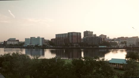 A-sunrise-aerial-rising-over-trees-revealing-the-Cape-Fear-River-and-downtown-Wilmington,-North-Carolina