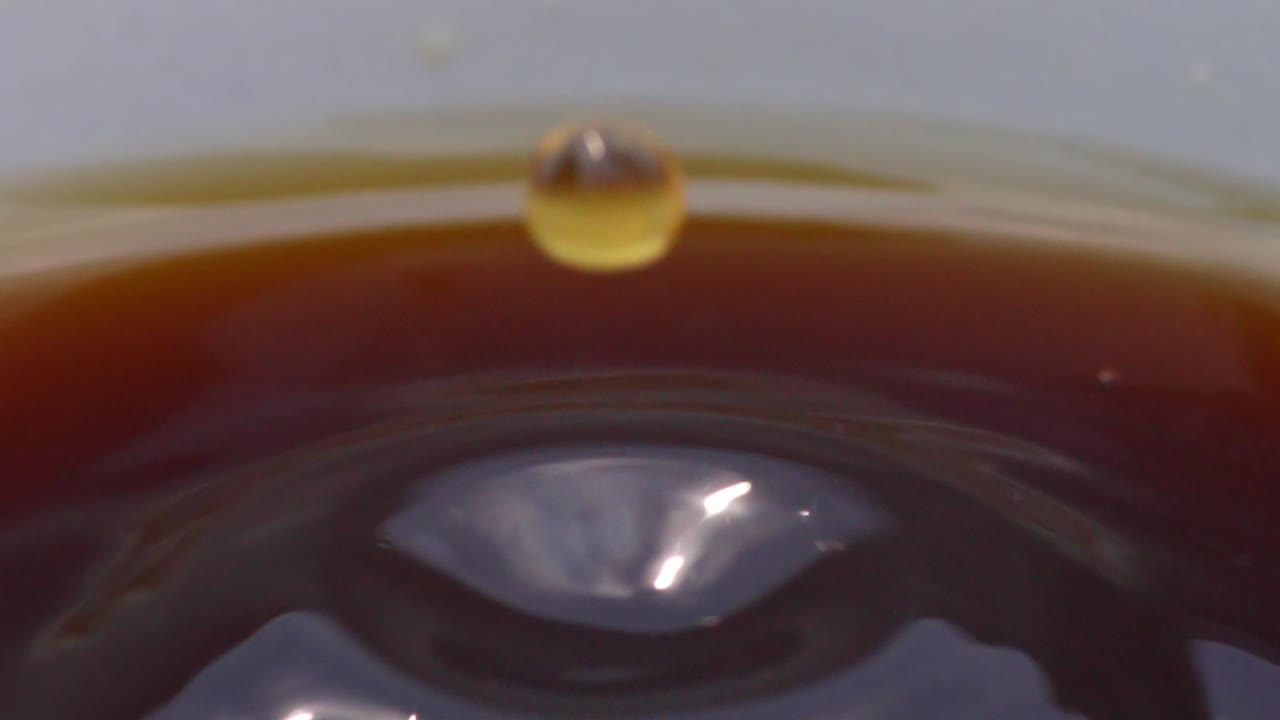 Drops of black coffee fall in slow motion into a glass splashing, close up macro view