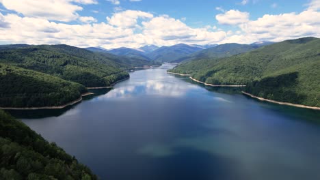 aerial shot of vidraru lake in romania. blue lake, dramatic curves, and green mountain backdrop in 4k.