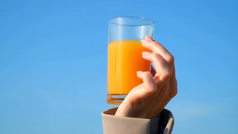 hand holding a glass of orange juice against a blue sky