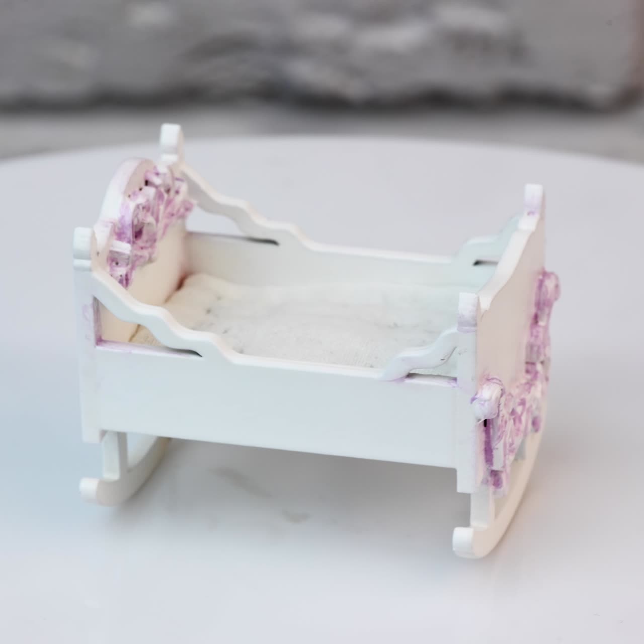 Culla bianca per una minuscola bambola alla filanda. Culla decorata con elementi intagliati colorati di rosa. Primo piano