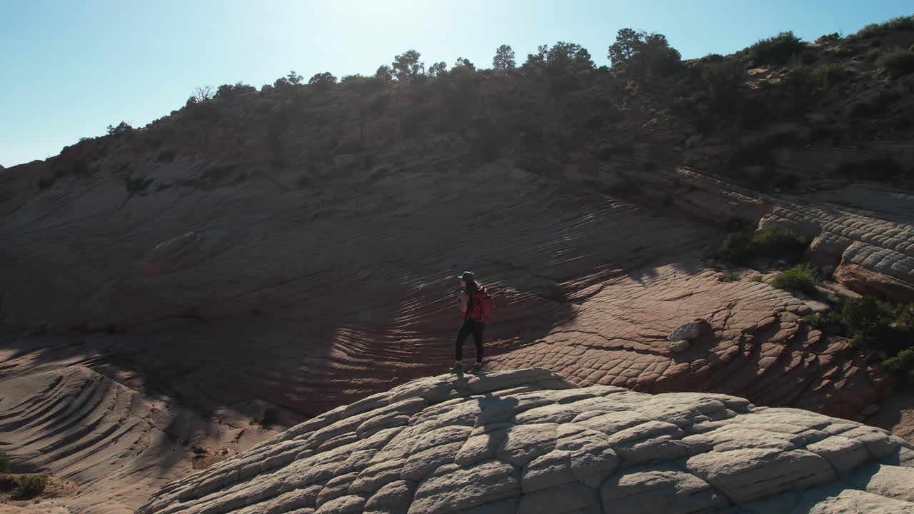 vista aérea de una excursionista con mochila en la cima de una colina y patrón de arenisca del desierto de utah, disparo de un dron en órbita