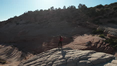 Aerial-View-of-Female-Hiker-With-Backpack-on-Top-of-Hill-and-Sandstone-Pattern-of-Utah-Desert,-Orbiting-Drone-Shot