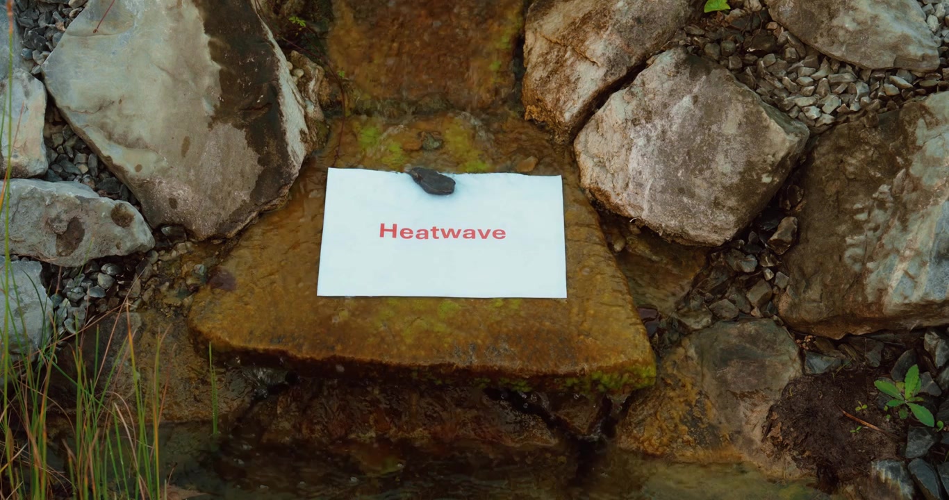 Acqua che scorre accanto a un cartello di ondata di calore, a illustrare il contrasto tra le risorse idriche e le temperature estive estreme. Ideale per concetti legati al cambiamento climatico, alla siccità e all'ambiente