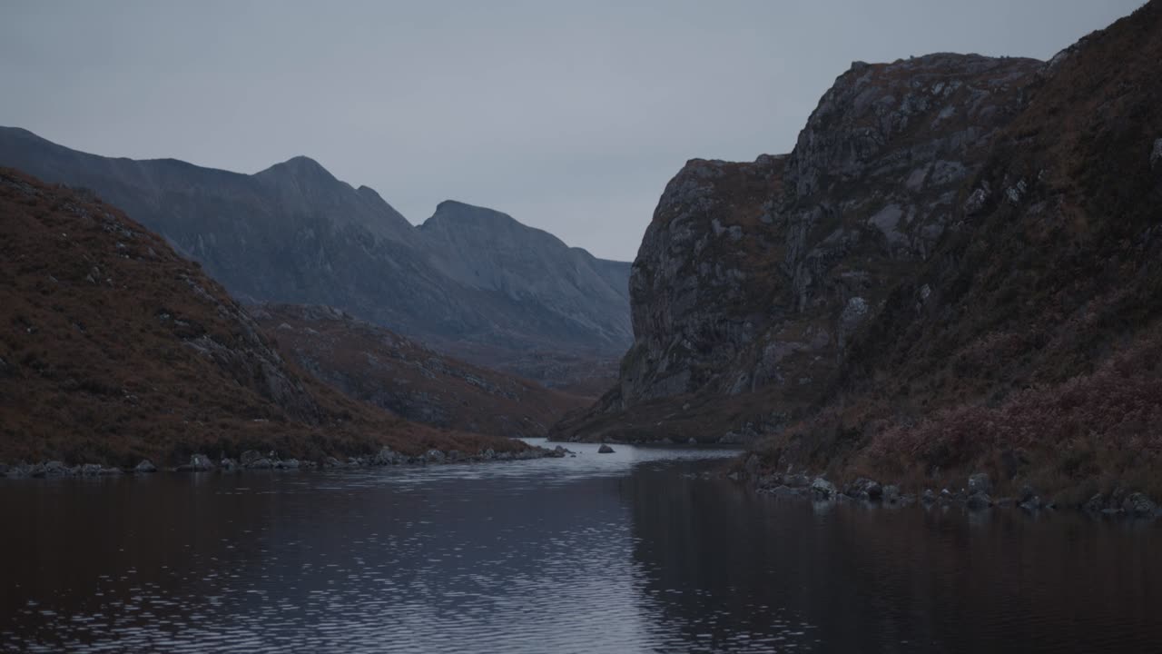 A still view of Loch na Thull in the Scottish Highlands. Rugged cliffs and sharp mountain peaks rise above calm water, forming a dramatic and remote wilderness landscape