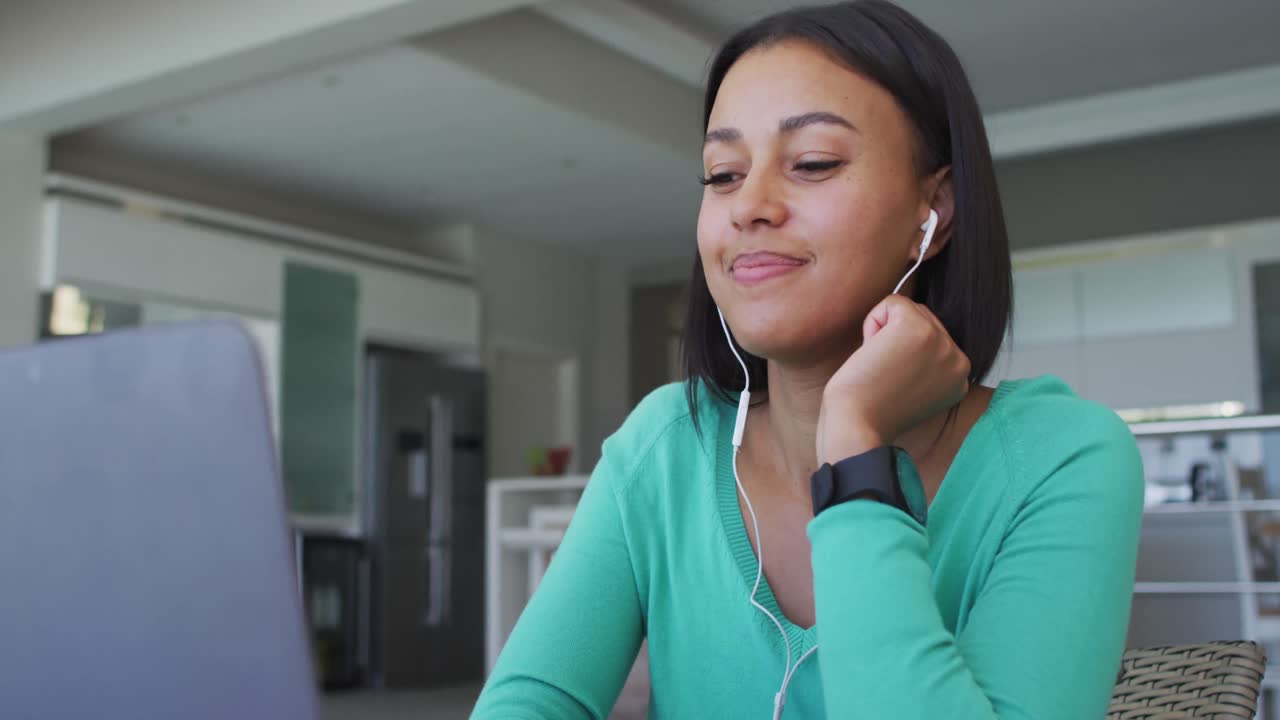 mujer afroamericana que usa auriculares usando una computadora portátil mientras trabaja desde casa