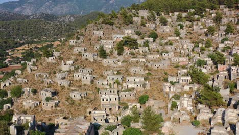 Luftdrohne,-Die-An-Einem-Sonnigen-Tag-Das-Verlassene-Historische-Geisterstadtdorf-Kayoy-Auf-Einem-Hügel-In-Fethiye,-Türkei,-Umkreist,-Während-Die-Sonne-über-Den-Zerstörten-Gebäuden-Untergeht