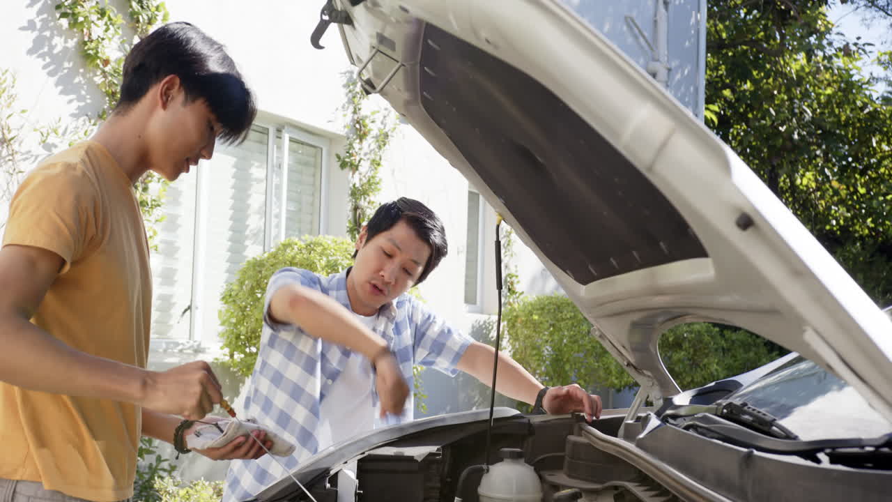 Asian father and teenage son working together on car engine in driveway
