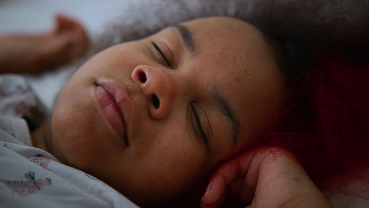 Peaceful sleep of a young woman with red hair, lying on a white pillow with her hands near her face, enjoying a moment of tranquility and rest