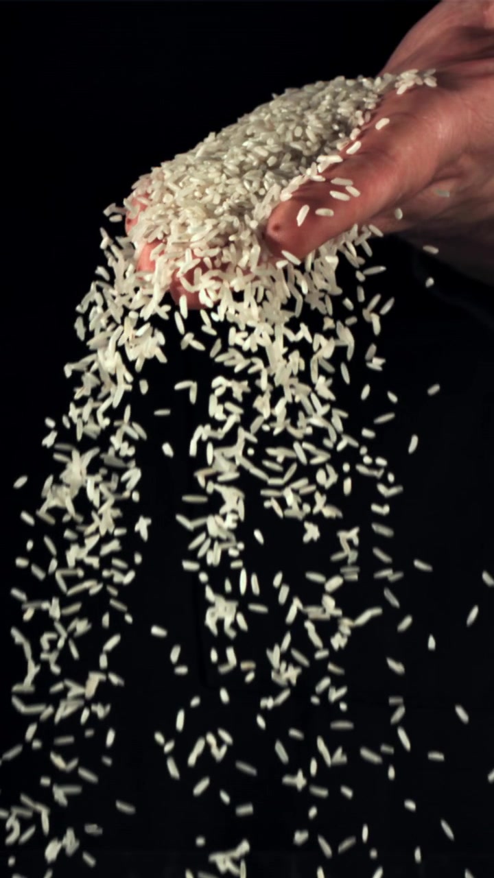 Grani di riso bianco che cadono da una mano al rallentatore