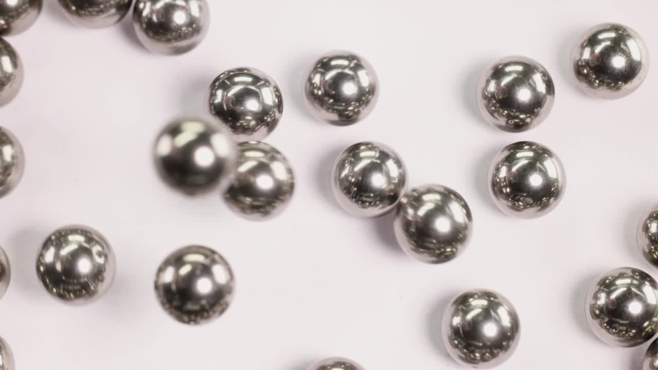 Ball bearings fall and collide in a macro close-up, highlighting their metallic texture and dynamic movement